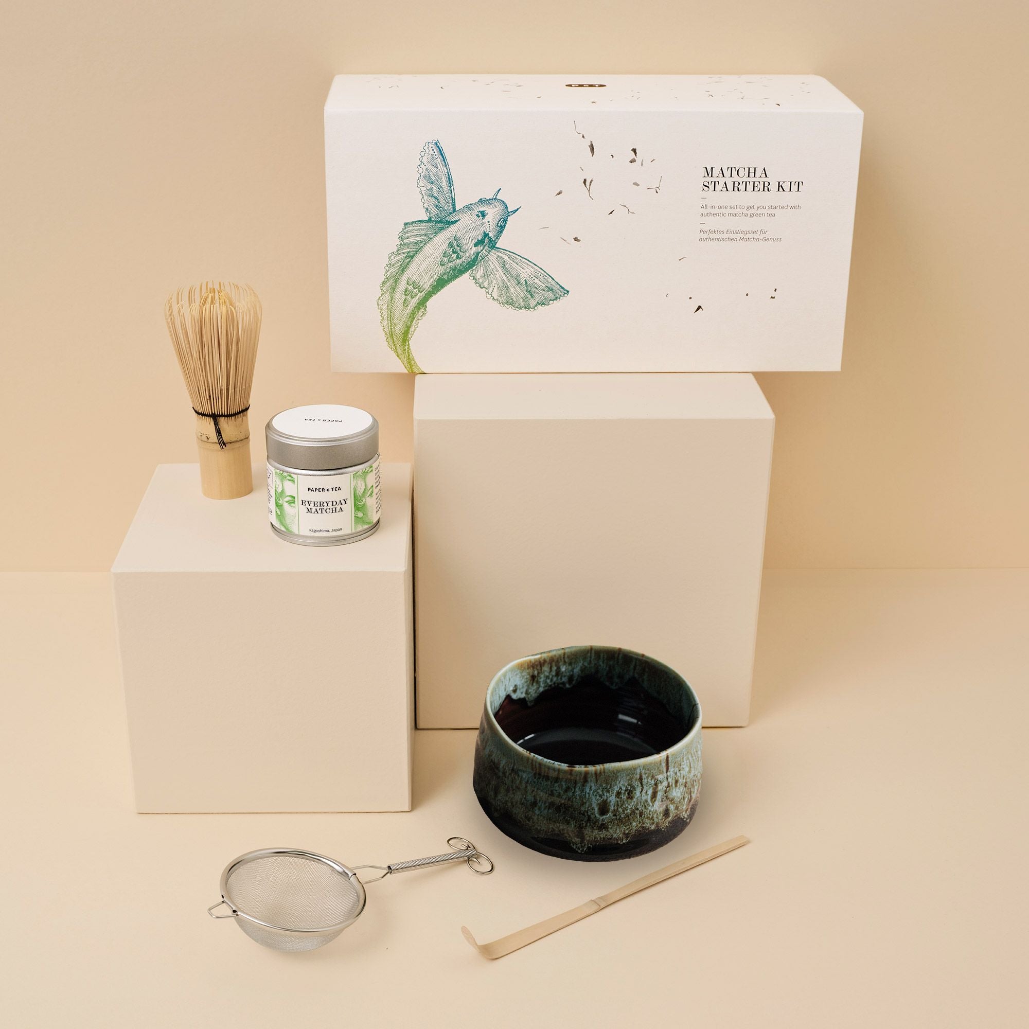 Matcha Starter Kit mit Bambusbesen, Teedose, Keramikschale, Sieb und Löffel vor beigem Hintergrund.