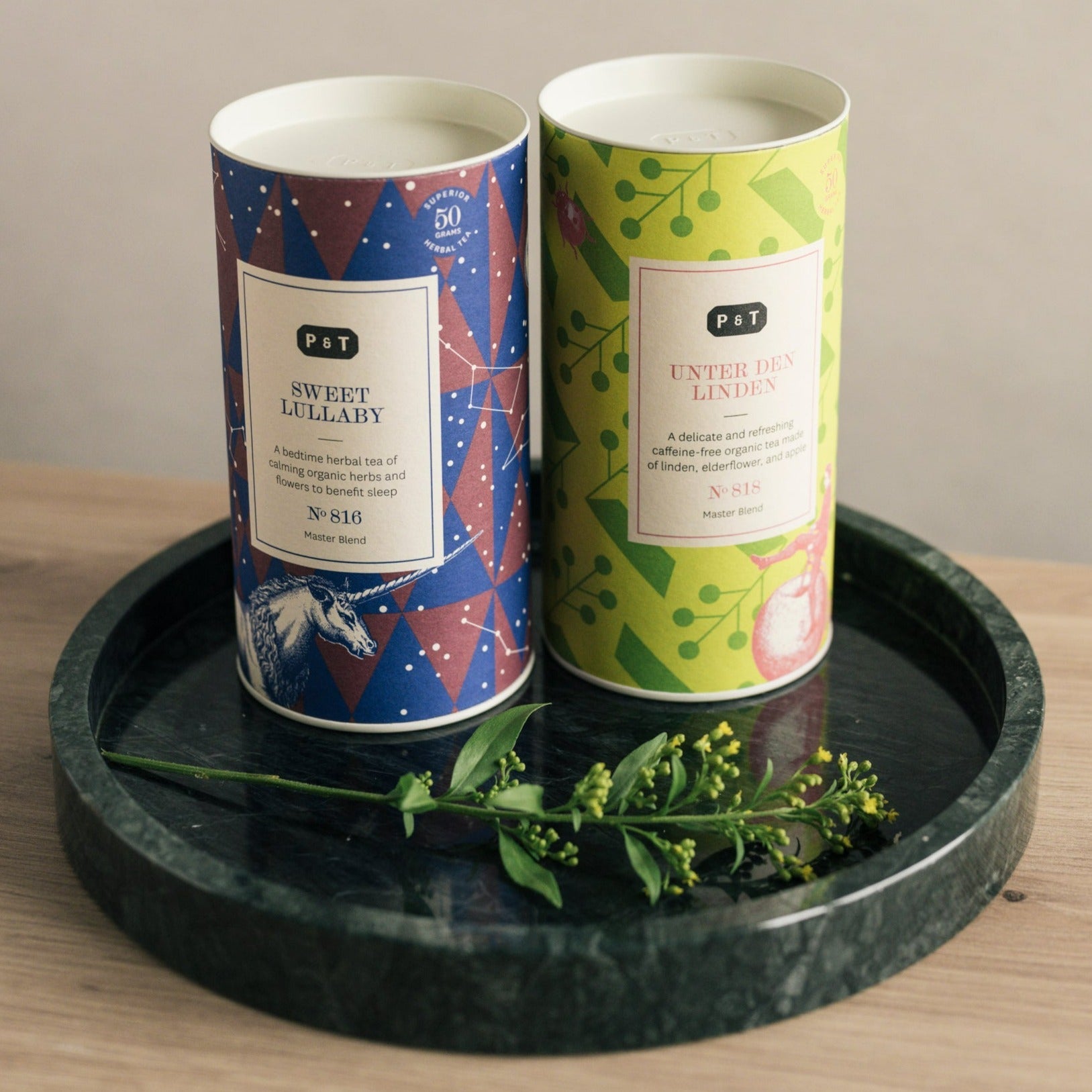 Zwei zylindrische Dosen mit Sweet Lullaby und Unter den Linden Bio-Kräutertees auf grünem Marmortablett.