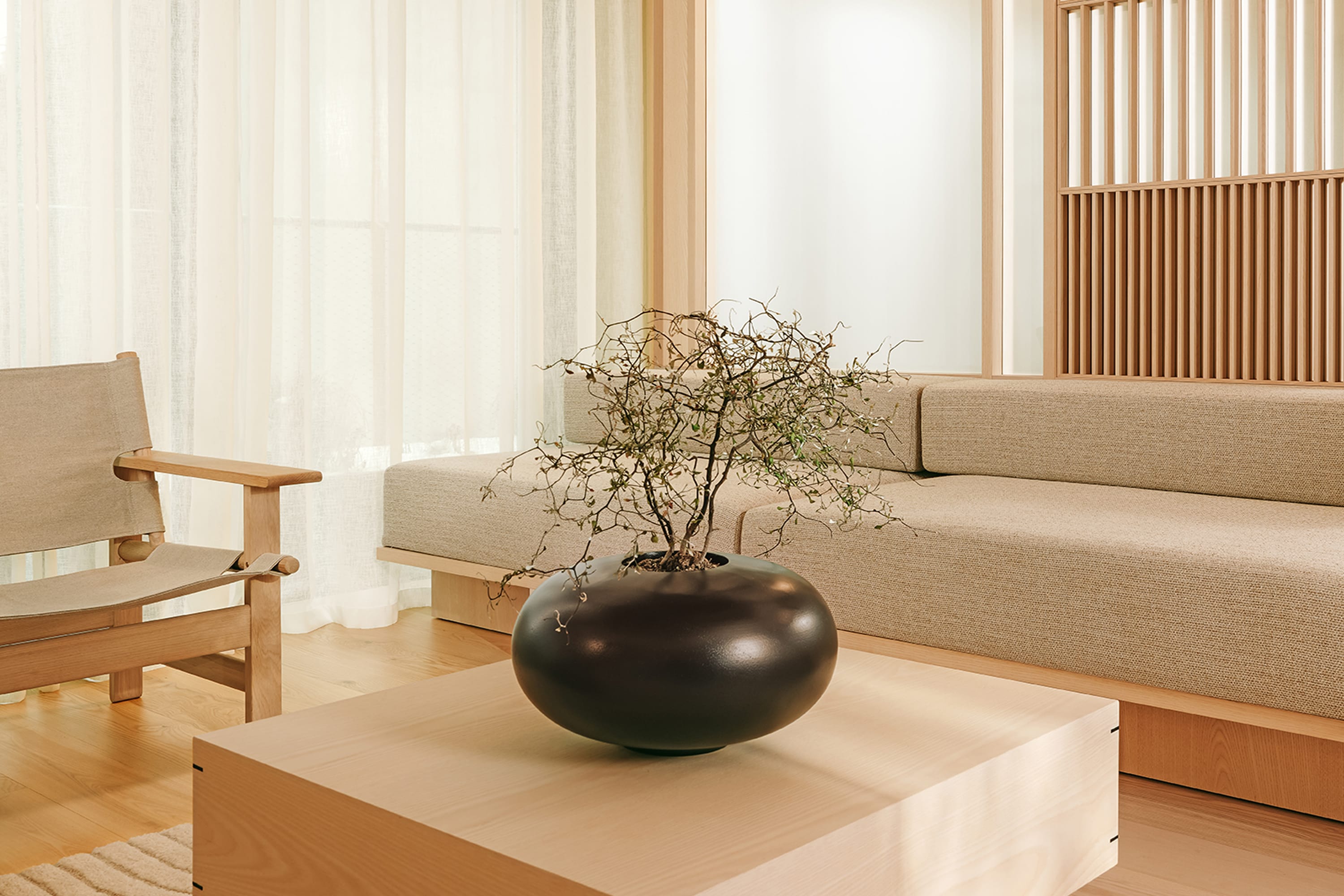 Minimalistisches Wohnzimmer mit hellem Holztisch, schwarzer Vase und beigem Sofa in beruhigendem Design.