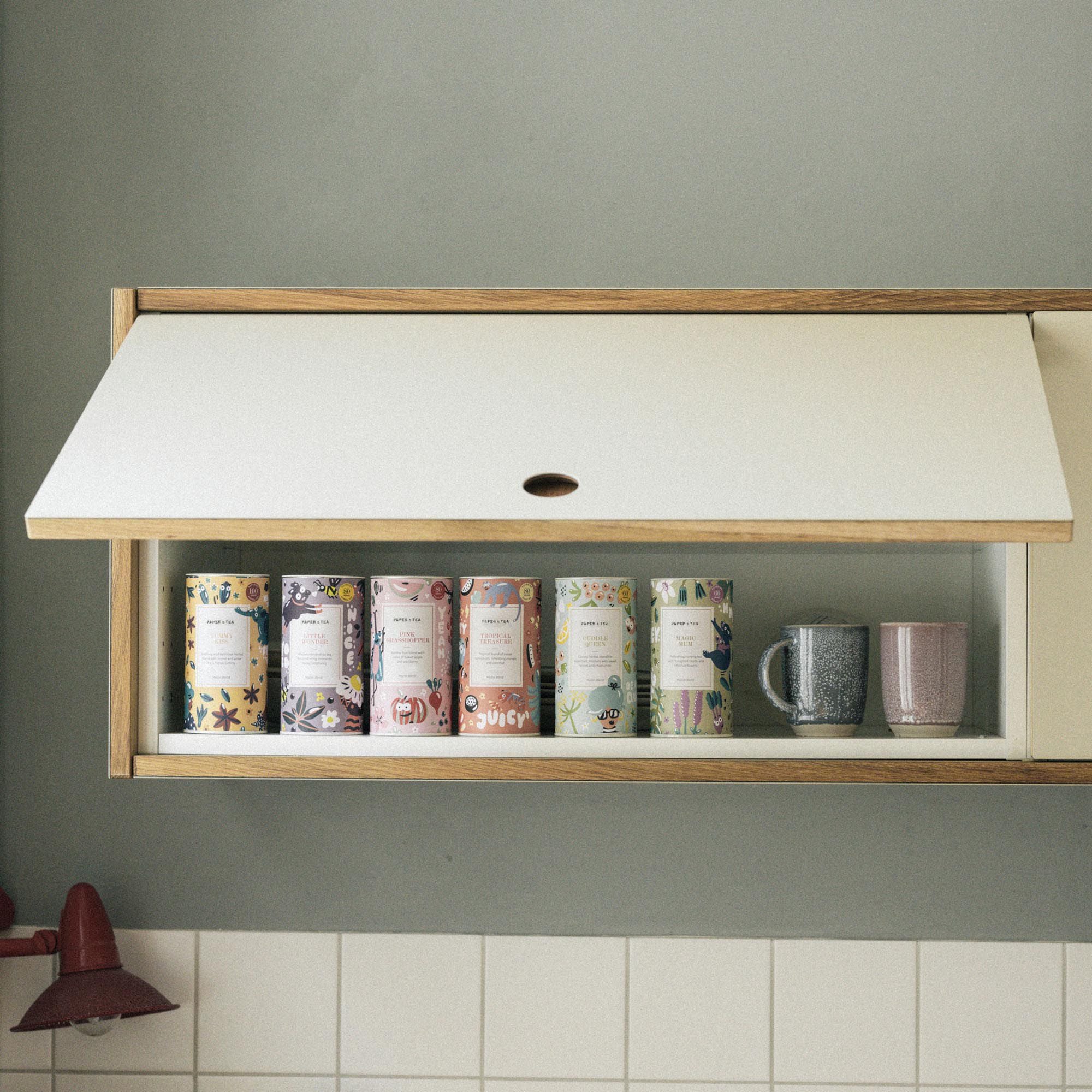 Holzregal mit bunten Tea-Dosen und Keramiktassen in gemütlicher Küchenecke