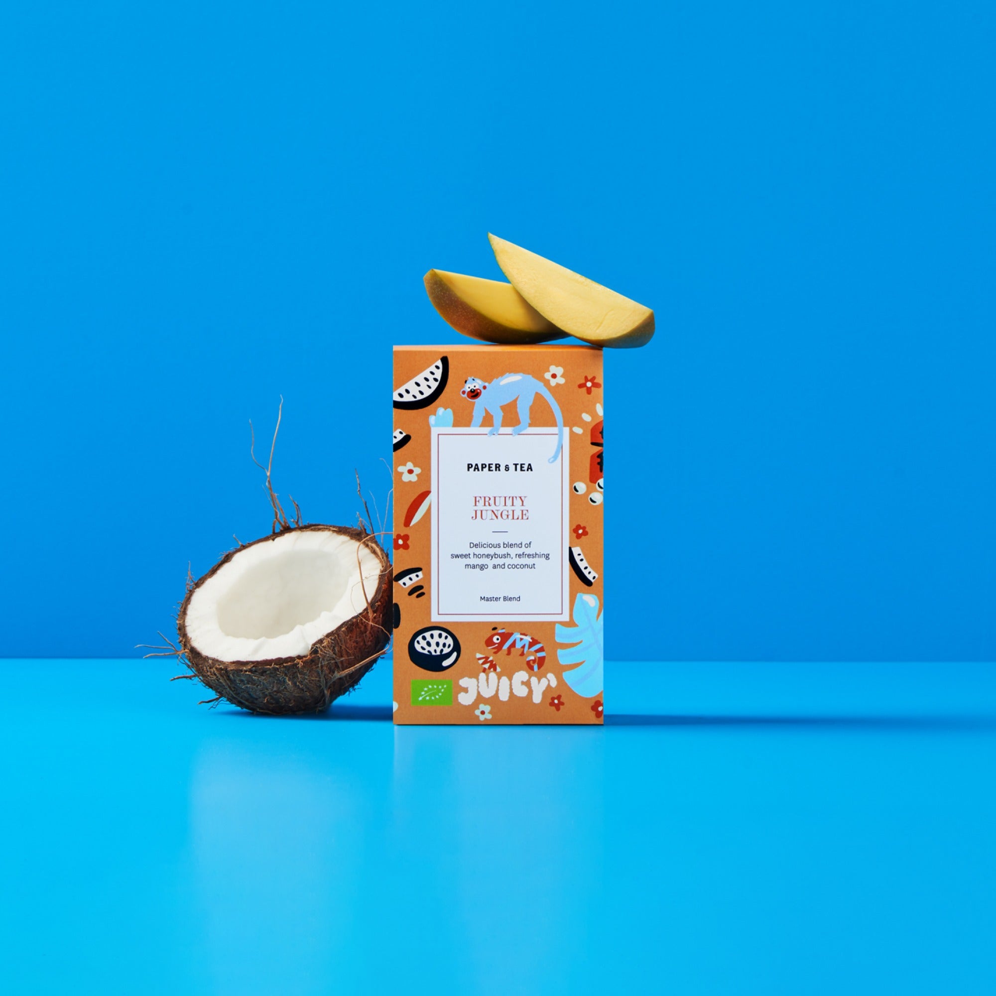 Orangefarbene Tee-Sammelbox mit Mango- und Kokosnussstücken vor blauem Hintergrund.