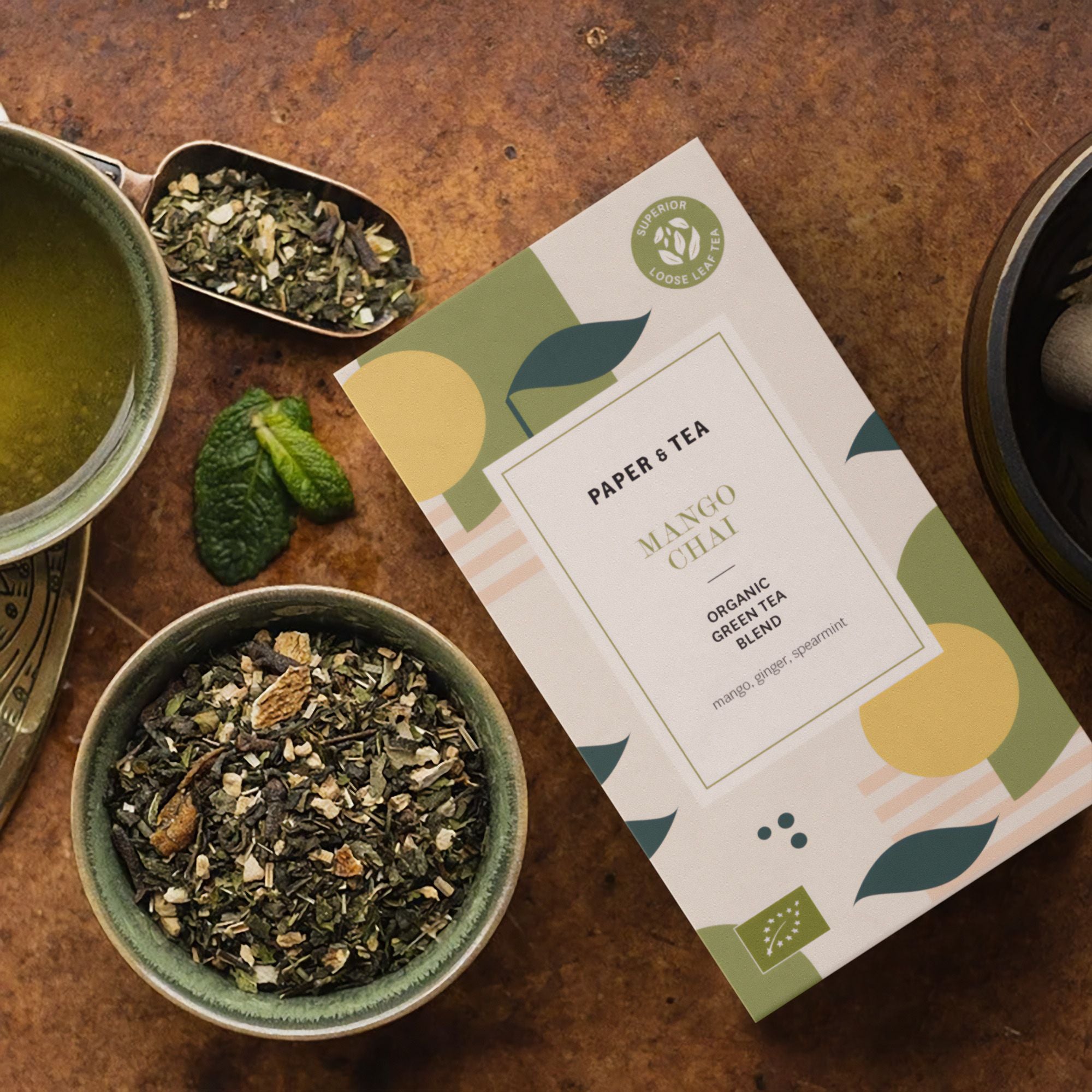 MANGO CHAI BIO Grüntee von PAPER & TEA in künstlerischer Verpackung, mit losen Teeblättern und Minze.