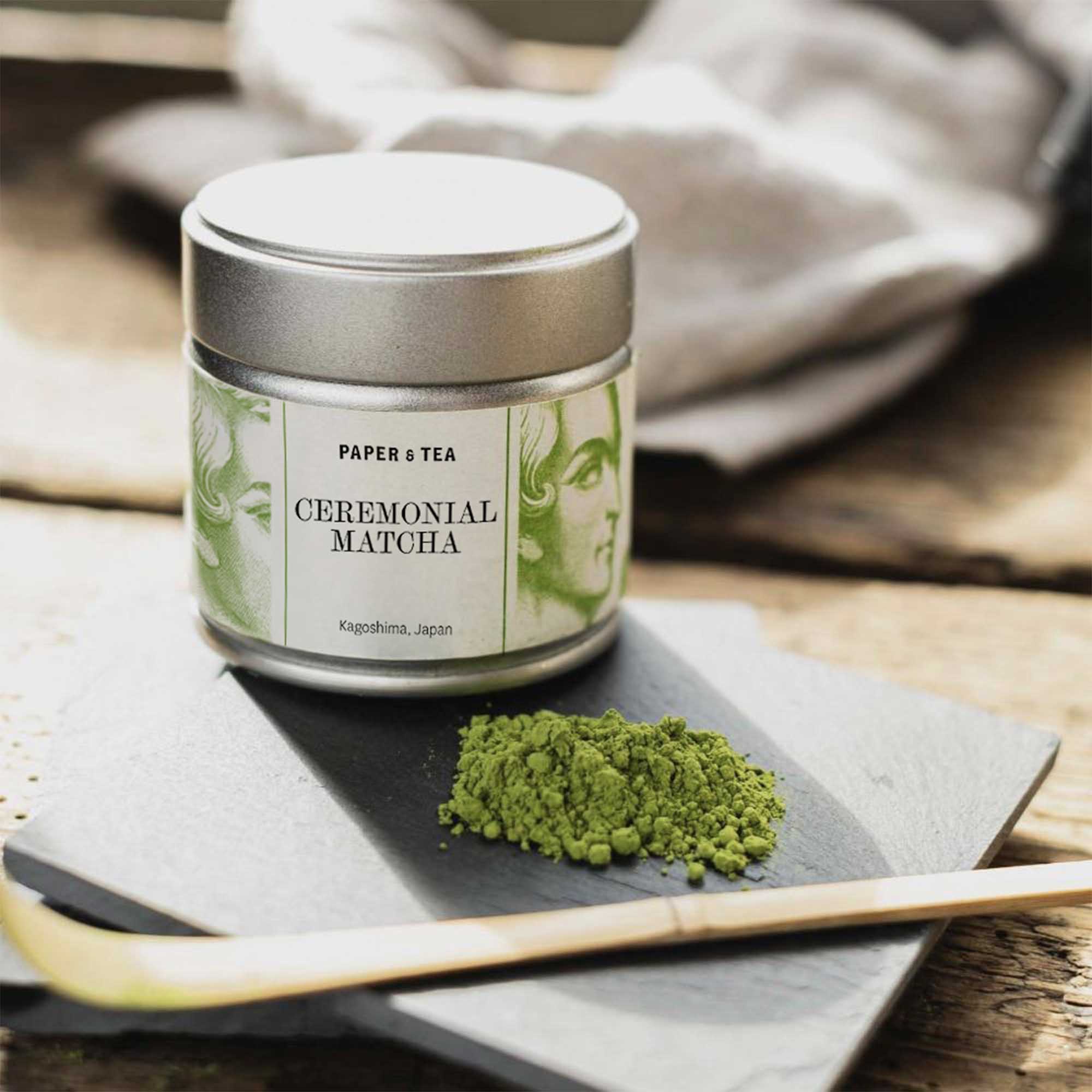 Metalldose mit Tee Ceremonial Matcha aus Kagoshima auf Schieferplatte, daneben grünes Matcha-Pulver und Bambuslöffel.