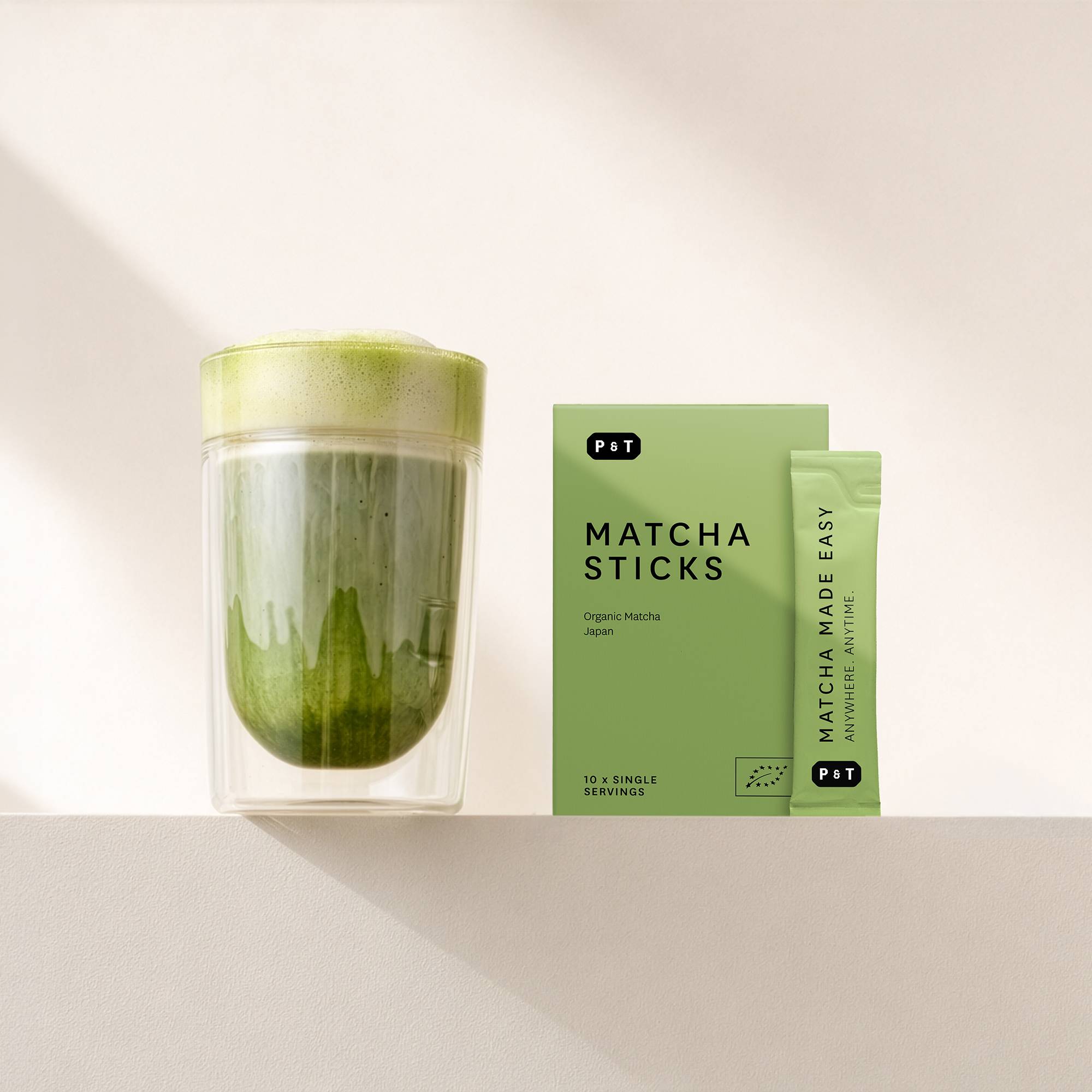 Doppelwandiges Glas mit schaumigem Matcha-Tee neben einer grünen P&T Matcha Sticks Box.