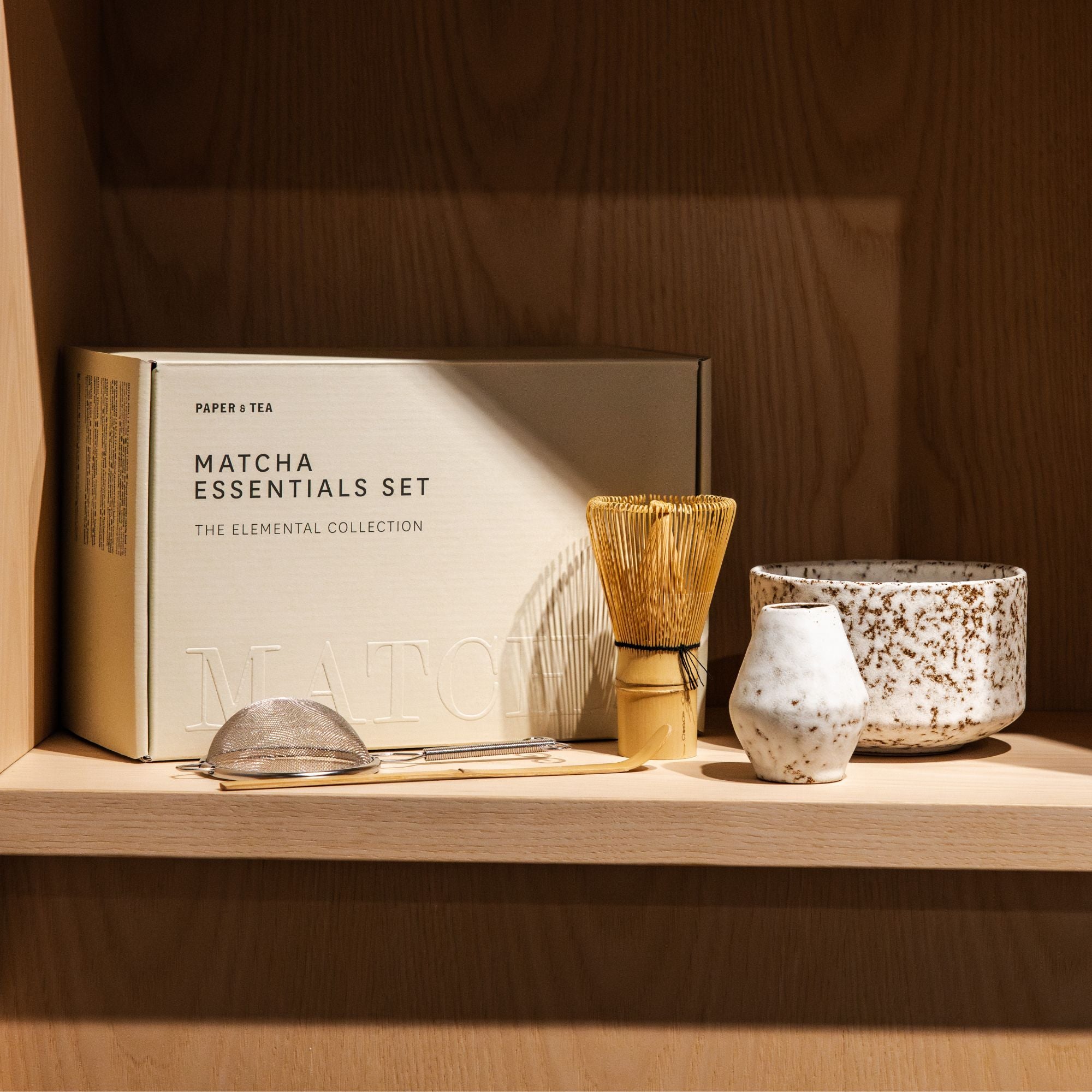 Elegantes Matcha Essentials Set mit Bambusbesen, Löffel, Sieb und Keramikgefäßen auf Holzregal