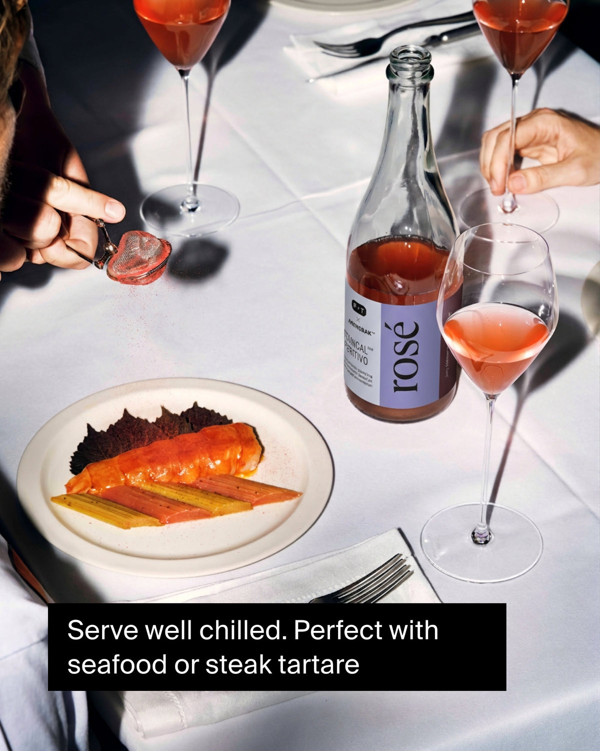 Flasche Roséwein und drei Gläser auf einem Tisch mit Meeresfrüchten und Gewürzstreuer