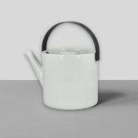 Moderner weißer Teekessel mit schwarzem Griff und kurzem Ausguss auf grauem Untergrund