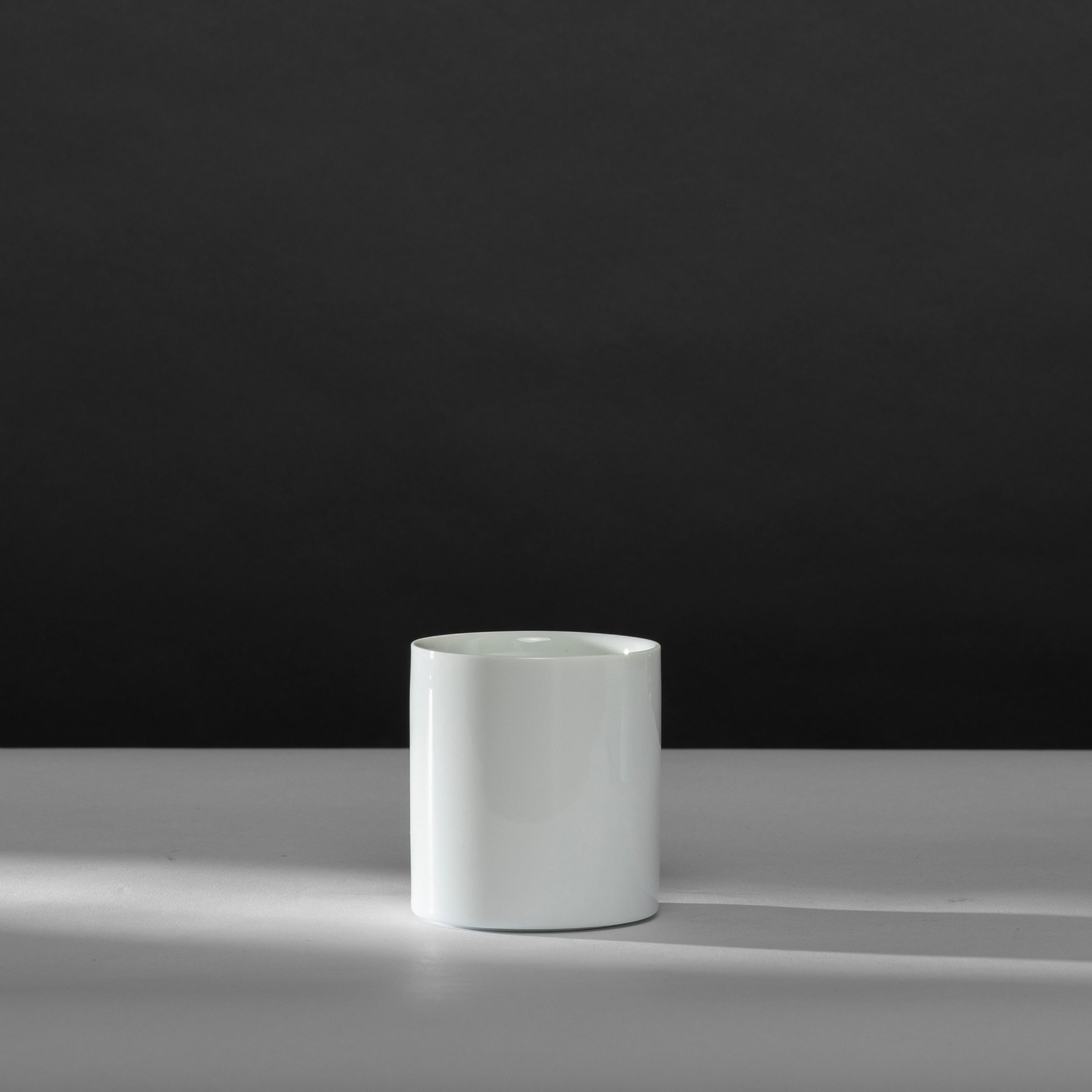 Weißer Keramikbecher mit glänzender Oberfläche auf grauem Untergrund, minimalistisches Design.