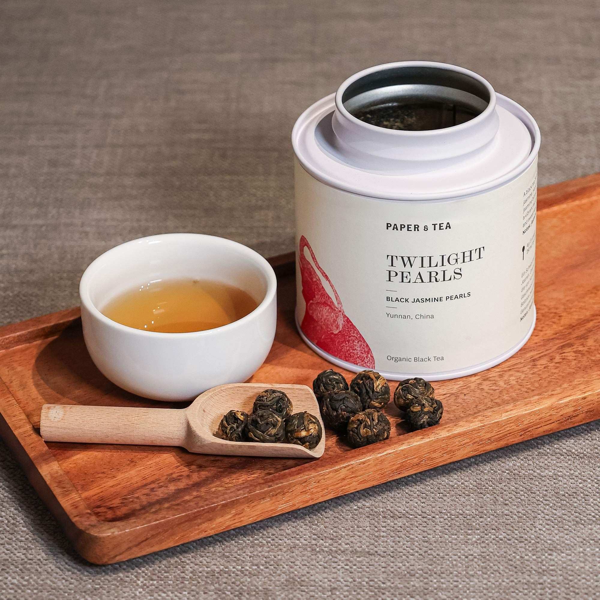 Weißer Behälter mit Organic Black Tea ‚Twilight Pearls‘, Tasse Tee und Teelöffel auf Holztablett