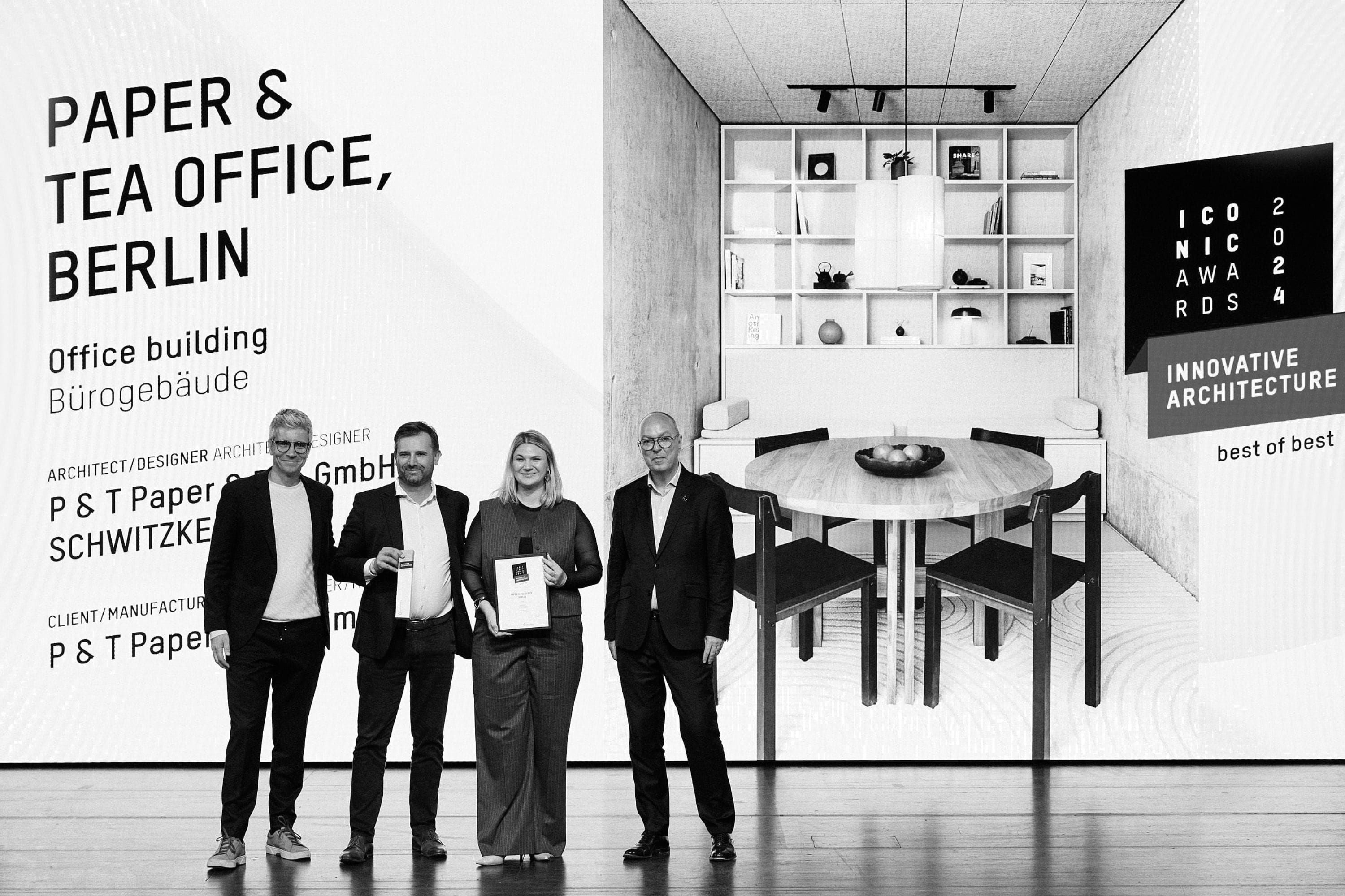 Vier formell gekleidete Personen mit Auszeichnungen vor dem beleuchteten P&T Büro Berlin