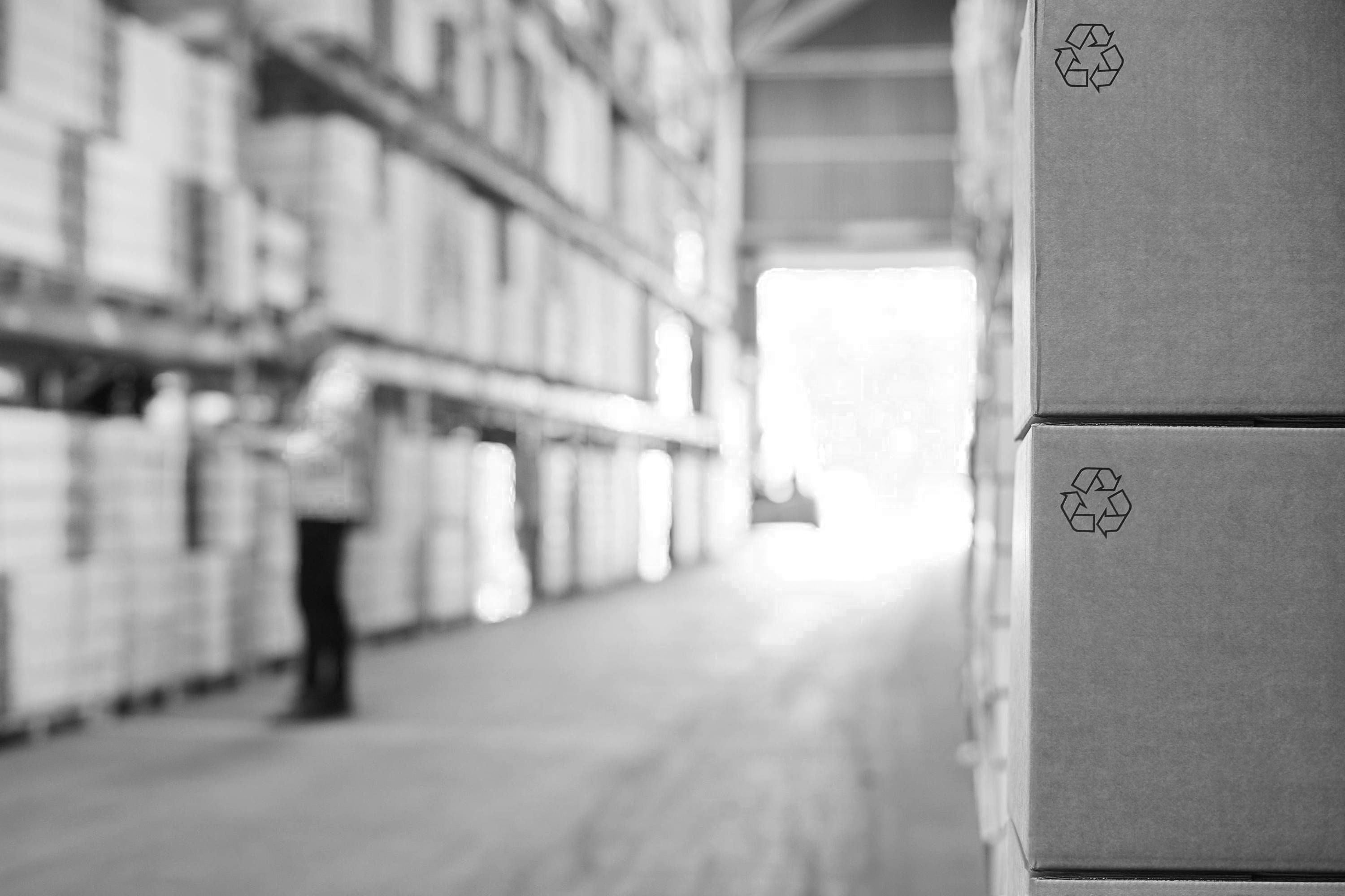 Lagergang mit hohen Regalen voller Kartons und einem Stapel Kartonboxen