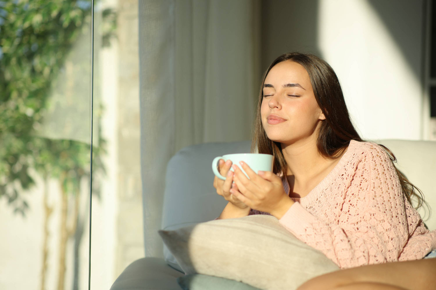 Junge Frau entspannt auf dem Sofa, hält eine hellblaue Tasse in der Hand