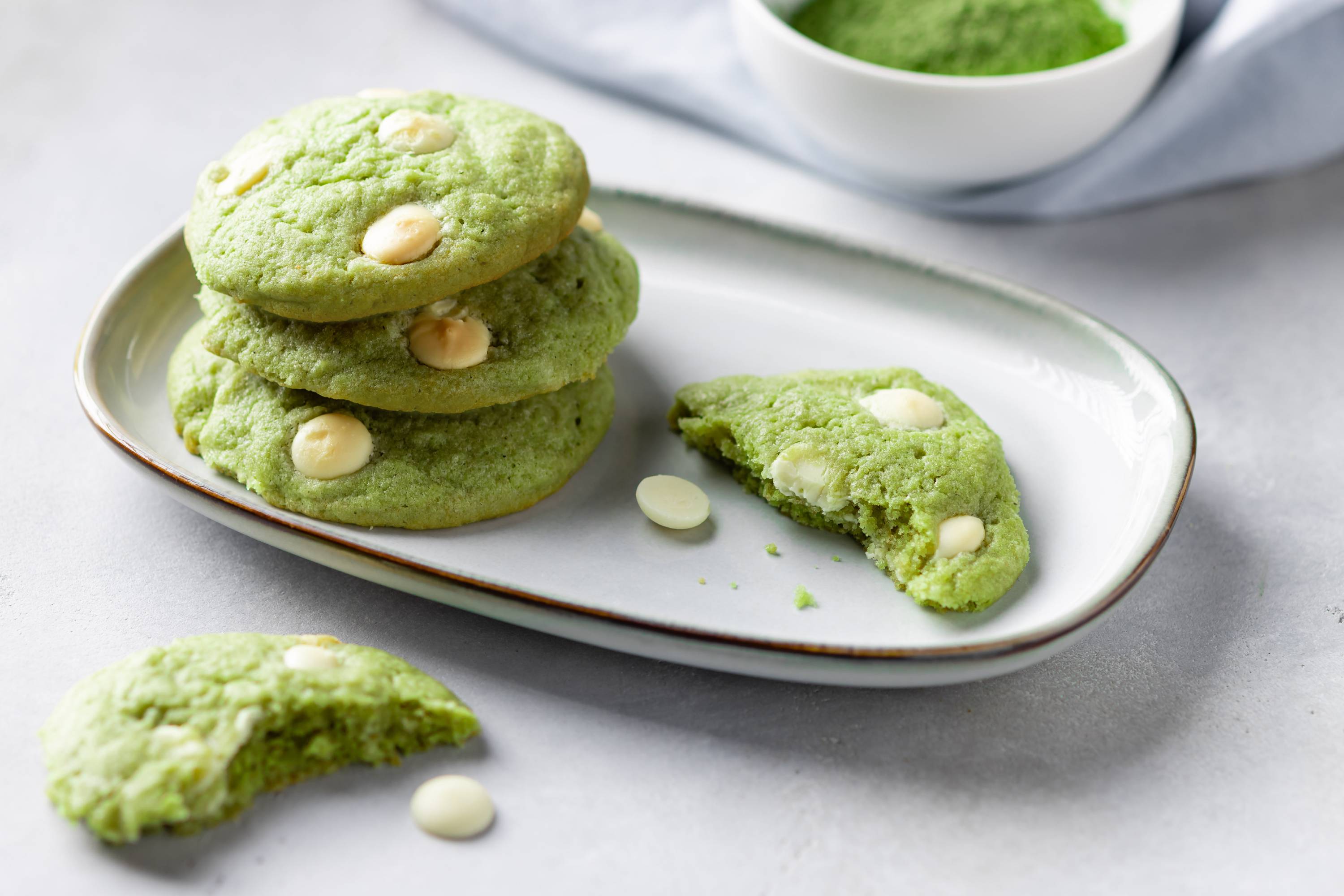 Drei grüne Matcha-Kekse mit weißen Schokoladenstückchen auf einem Teller