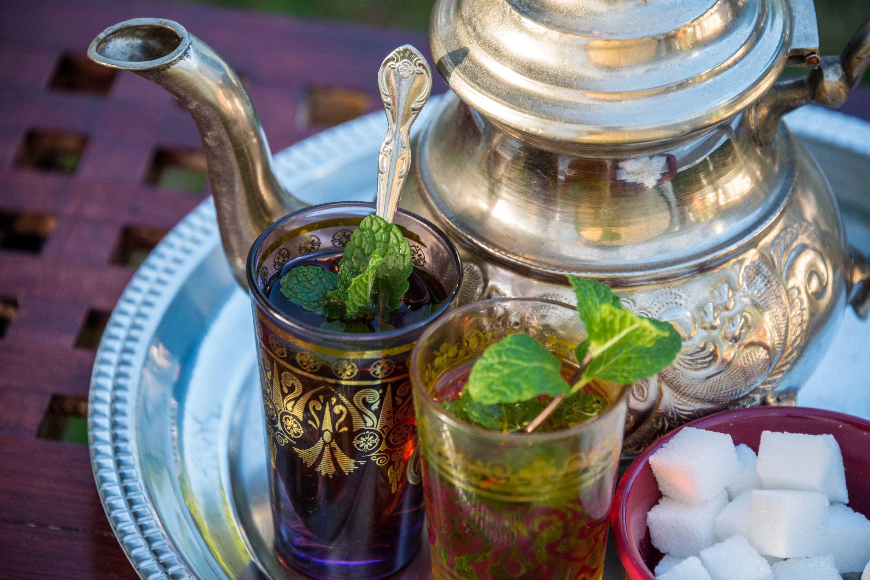 Zwei kunstvoll verzierte Teegläser mit frischer Minze, silberner Teekanne und Zuckerwürfeln