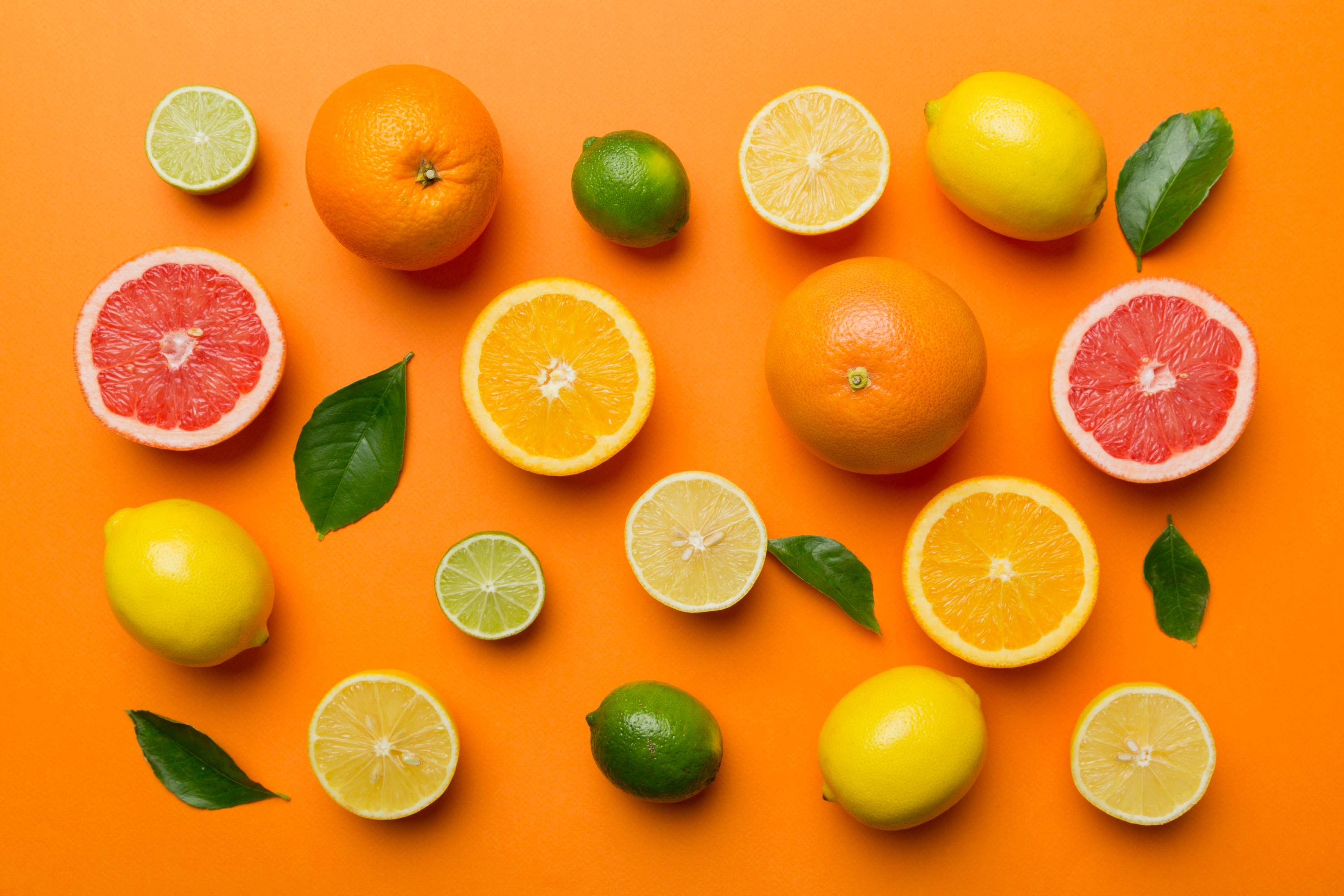 Vitamin C reiche Orangen, Limetten, Grapefruits, Zitronen und grüne Blätter auf orangefarbenem Hintergrund