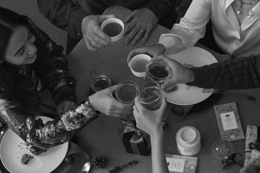 Vier Personen stoßen mit Gläsern an, umgeben von P&T Tees und Schokolade auf einem festlich gedeckten Tisch