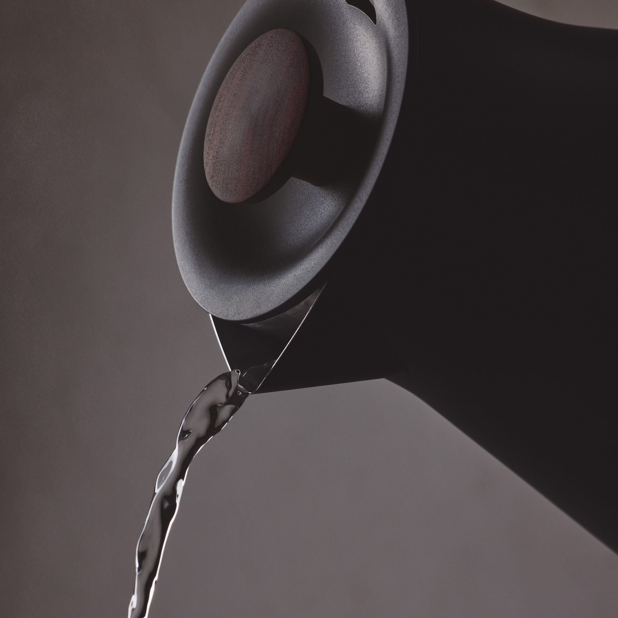 Eleganter schwarzer Wasserkocher mit spitzem Ausguss, der klares Wasser auf grauem Hintergrund gießt.