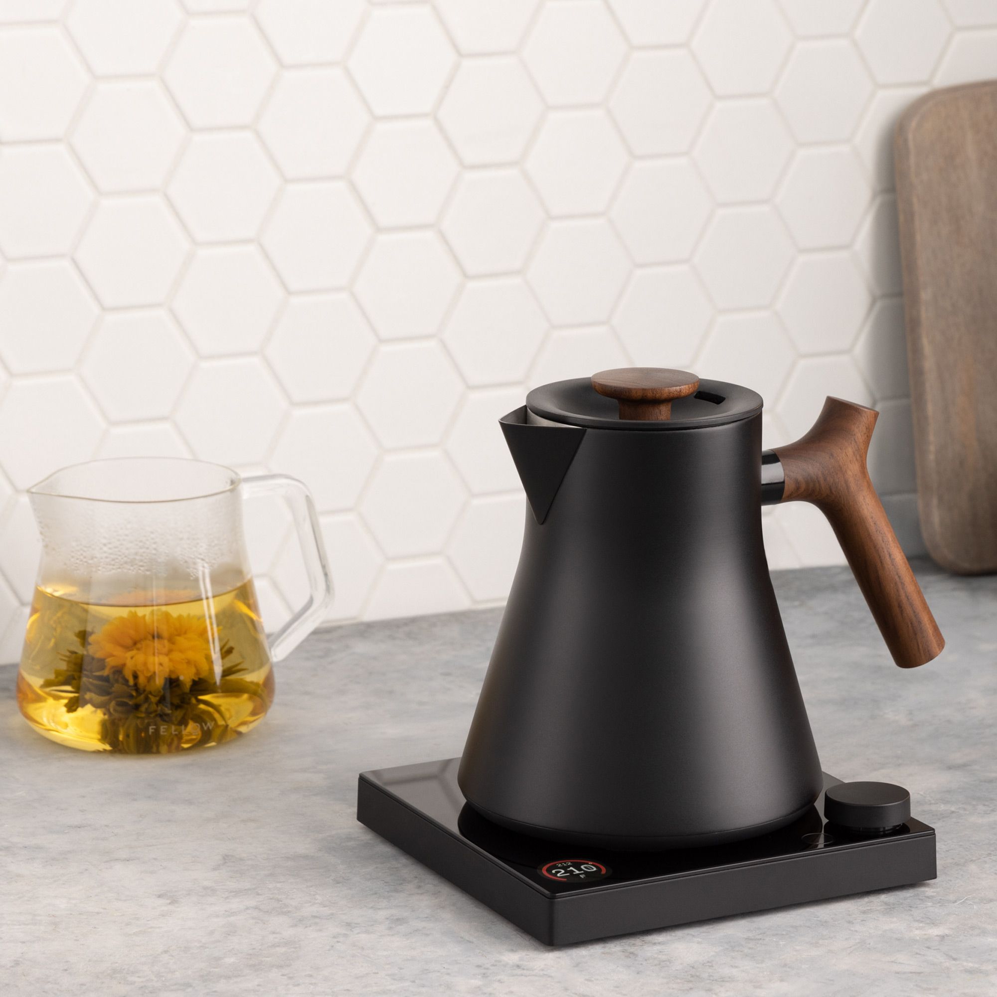 Moderner matt-schwarzer Wasserkocher mit Holzgriff und digitaler Anzeige neben Glas-Teekessel mit gelbem Tee.