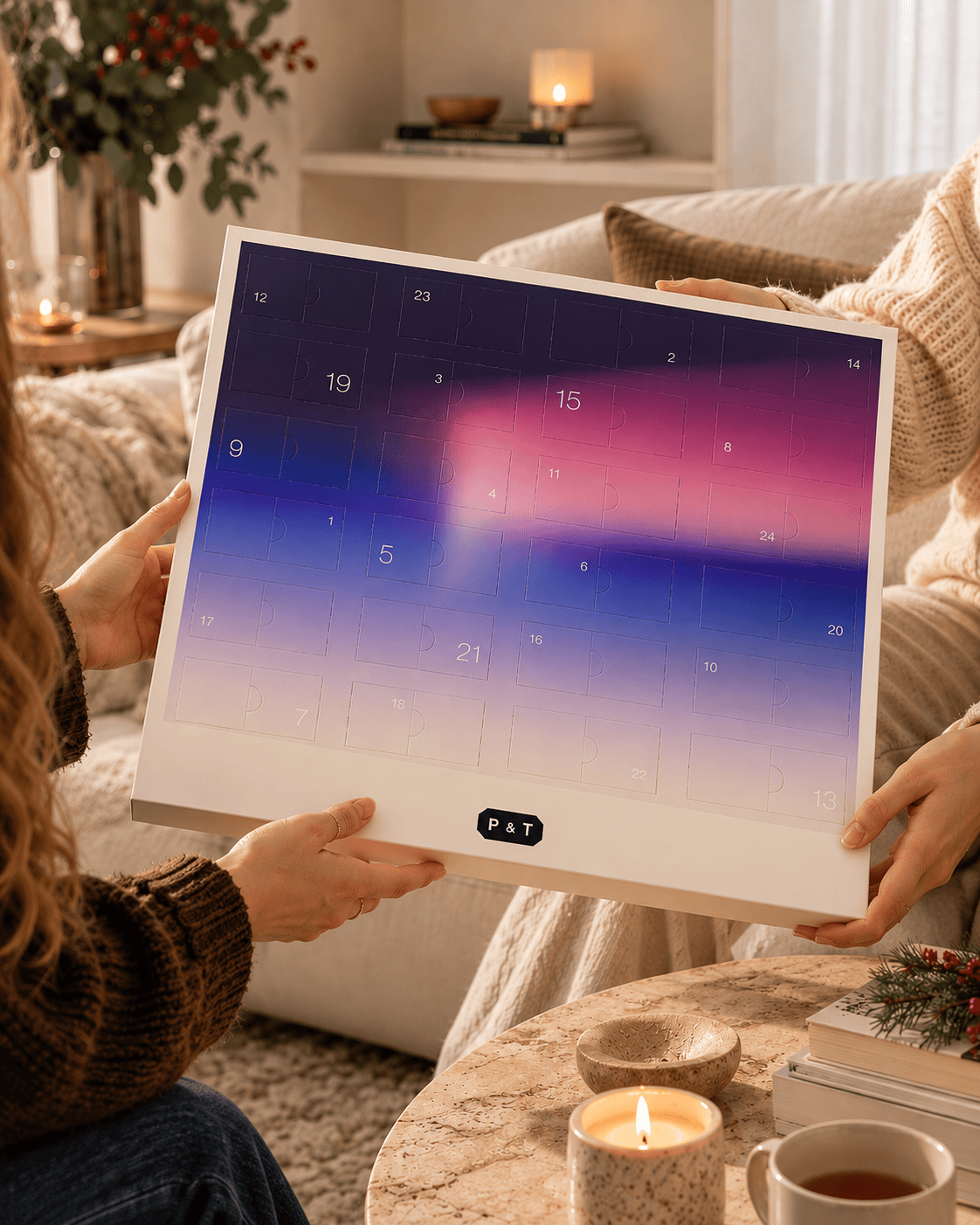 Zwei Frauen halten bunte P&T Adventskalender mit Zahlen 1 bis 24 im gemütlichen Wohnzimmer