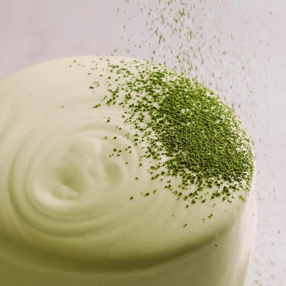 Runder, hellgrüner Matcha-Kuchen mit Zuckerguss und bestreutem Matcha-Pulver