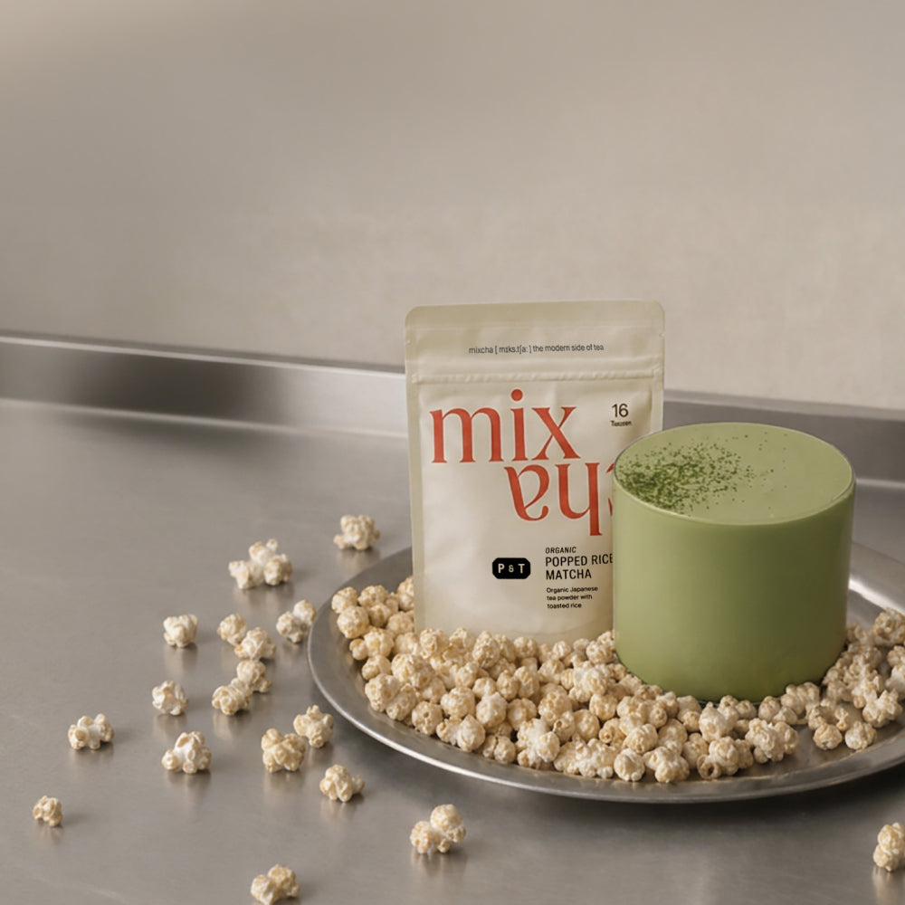 Beige Tasche mit 'mix ey' Bio Reismatcha-Pulver auf Tablett, grünem Matcha-Getränk und Reispuffs.