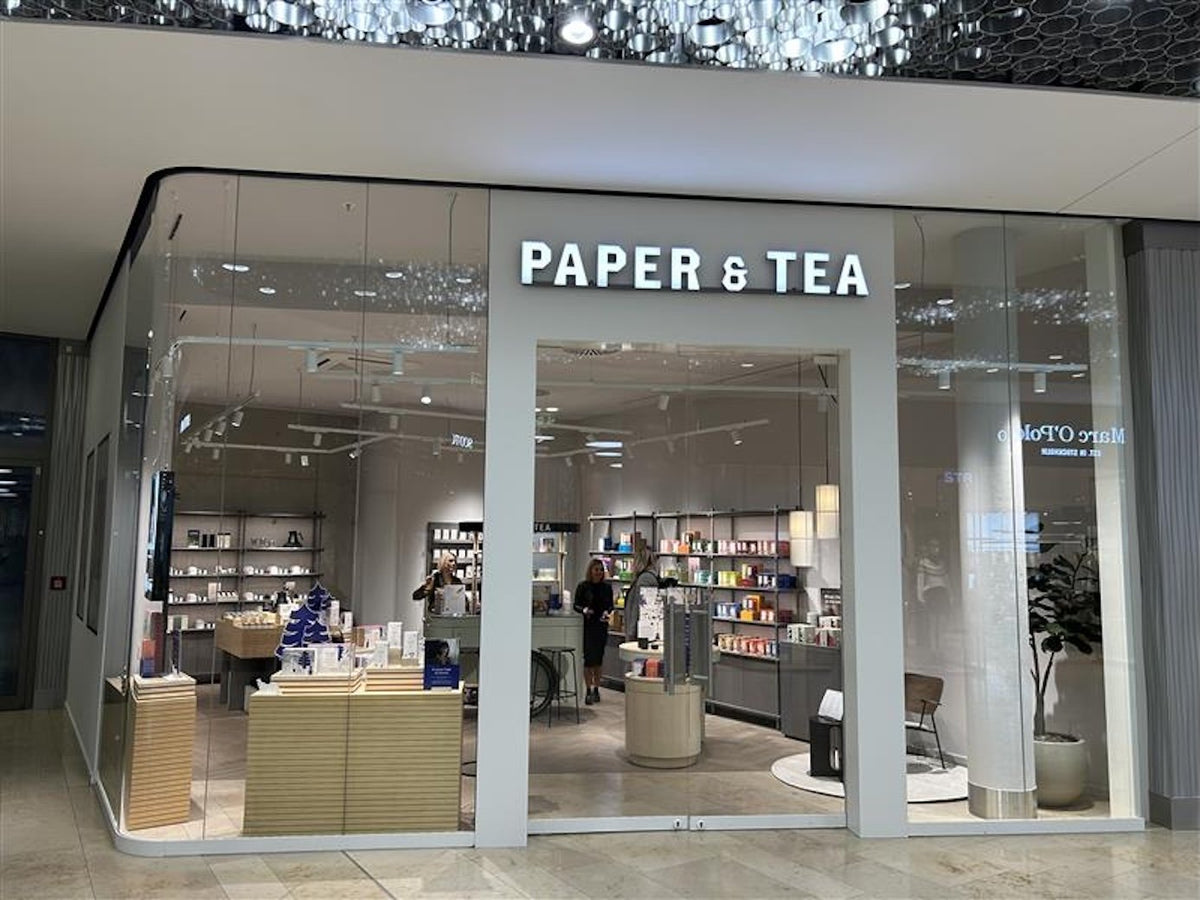 Moderner PAPER & TEA Laden mit Glaswänden, beleuchtet und mit Teeboxen und Papierwaren ausgestattet