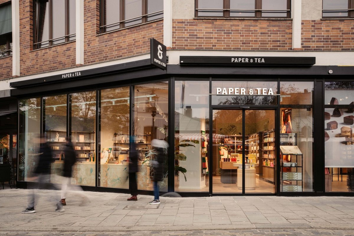 Modernes Paper & Tea Geschäft mit großen Fenstern und schwarzem Rahmen an einer Backsteinecke.